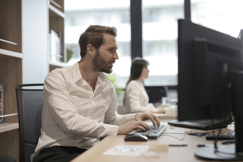System engineer aan het werk in modern kantoor Man aan het werk op computer in een professioneel IT-kantoor met collega op de achtergrond